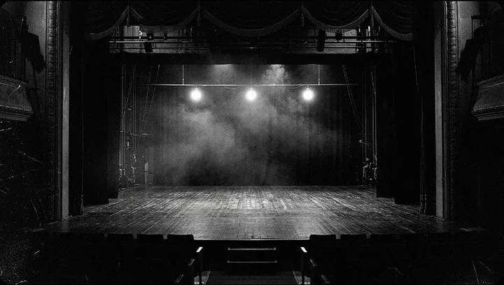 An empty theater stage lit by three backlights through haze